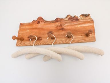 A wooden wall-mounted coat rack with four pegs and three padded fabric hangers at Shipton Hill View in Shipton Gorge