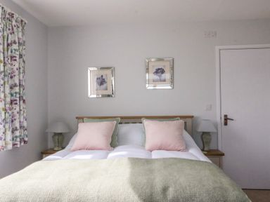 A bedroom with a bed with pillows a green blanket floral curtains and two framed pictures on the wall at Shipton Hill View in Shipton Gorge