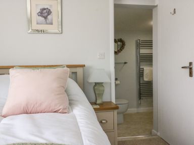 A bedroom with a bed a pink pillow a bedside table with a lamp and an open door leading to a bathroom at Shipton Hill View in Shipton Gorge