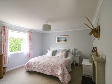 A bedroom with a bed with patterned bedding bedside tables and a window with pink curtains at Shipton Hill View in Shipton Gorge