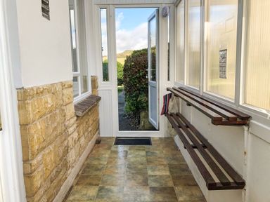 A hallway with tiled floor stone wall and wooden bench by a door leading outside at Shipton Hill View in Shipton Gorge