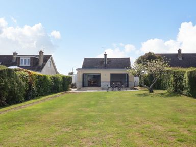 A backyard with a lawn hedge a tree and a house with an outdoor table and chairs at Shipton Hill View in Shipton Gorge