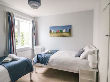 A bedroom with two single beds blue throws on beds chair near window and painting on wall at Shipton Hill View in Shipton Gorge