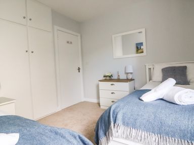 A bedroom with beds covered in blue blankets a white dresser a mirror on the wall and a door at Shipton Hill View in Shipton Gorge