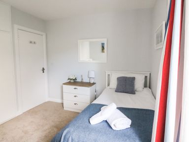 A bedroom with a single bed a bedside table a mirror and a window with striped curtains at Shipton Hill View in Shipton Gorge