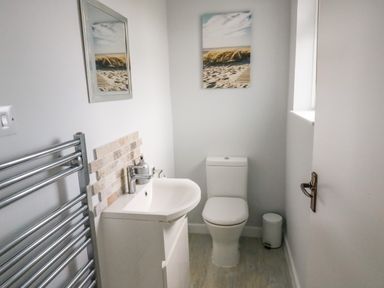A bathroom with a toilet a sink a towel rack and a beach-themed picture on the wall at Shipton Hill View in Shipton Gorge