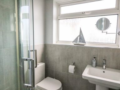 A bathroom with a glass shower door toilet sink and window with a round mirror at Shipton Hill View in Shipton Gorge