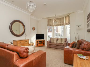 A living room with two brown leather sofas a brown fabric loveseat a wooden cabinet a round mirror and a television at Sea Star in Weymouth