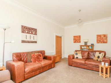 A living room with two brown leather sofas cushions a bookshelf and artworks on the walls at Sea Star in Weymouth