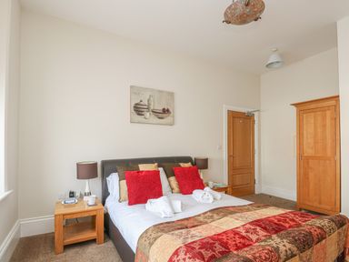 A bedroom with a double bed red and brown cushions wooden bedside tables lamps a wooden wardrobe and a wooden door at Sea Star in Weymouth