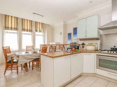 A kitchen with dining table and wooden chairs with striped blinds on windows at Sea Star in Weymouth
