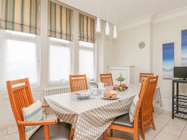 A dining room with a polka dot tablecloth on a table surrounded by wooden chairs with cushions at Sea Star in Weymouth