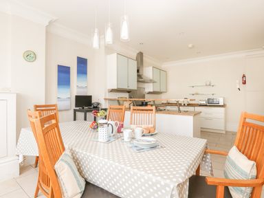 A kitchen and dining area with a table covered in a polka dot tablecloth and wooden chairs at Sea Star in Weymouth