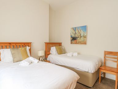 A bedroom with two single beds a small lamp a wooden chair and a painting of sailboats on the wall at Sea Star Weymouth