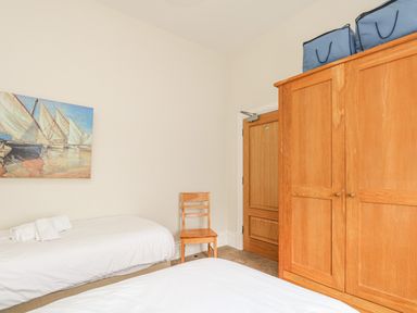A bedroom with two single beds a wooden chair a wooden wardrobe and a painting of boats on a wall at Sea Star in Weymouth
