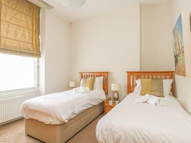 A bedroom with two single beds bedside tables lamps and a painting at Sea Star in Weymouth