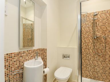 A bathroom with a sink toilet and a shower area with mosaic tiles at Sea Star in Weymouth