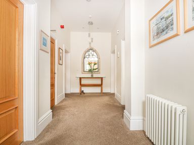 A hallway with wooden doors carpeted floor a radiator and a wooden table with flowers at Sea Star in Weymouth