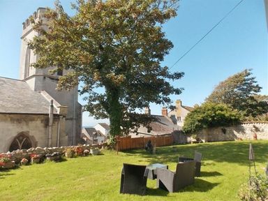 An outdoor garden area with chairs and a table near a large tree and stone building at St Johns View Portland