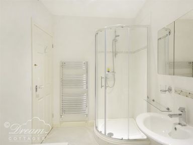 A bathroom with a corner shower enclosure a wall-mounted towel radiator and a sink with a mirror above at St Johns View in Portland