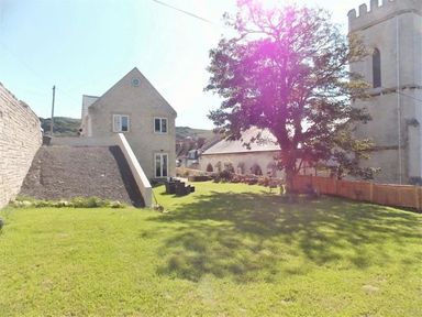 A lawn area with a tree and a seating area beside a stone house and a church at St Johns View in Portland