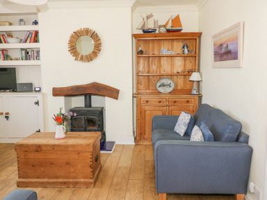 A living room with a blue sofa wooden coffee table and woodburner at Studland Cottage in Studland