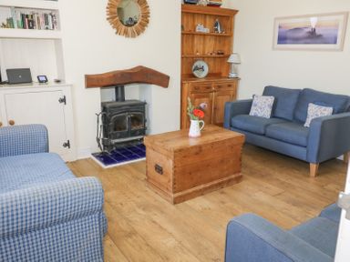 A living room with a wood stove a wooden chest as a coffee table two blue sofas a wooden cabinet and a bookshelf at Studland Cottage in Studland