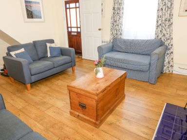 A living room with two blue sofas a wooden chest as a coffee table and a wooden door at Studland Cottage in Studland
