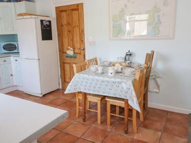A kitchen with a wooden table set for breakfast and a refrigerator next to a wooden door at Studland Cottage in Studland