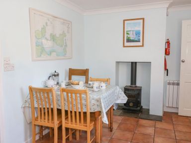 A dining area with a wooden table and chairs set with teacups and bread near a small wood stove at Studland Cottage in Studland
