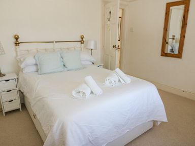 A bedroom with a double bed with white bedding and rolled towels on top at Studland Cottage in Studland