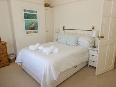 A bedroom with a bed with pillows and towels bedside tables with lamps and a chest of drawers at Studland Cottage in Studland