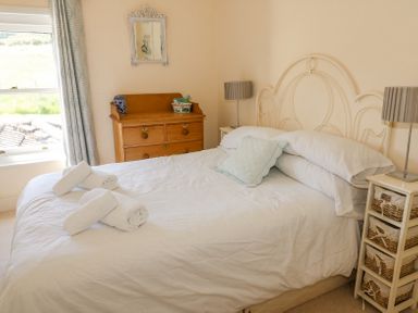 A bedroom with a white bed, rolled towels on the bed, a wooden chest of drawers, and bedside tables with lamps at Studland Cottage in Studland