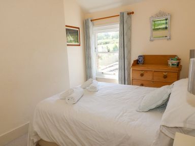 A bedroom with a bed with white linens and rolled towels next to a wooden dresser with decorative items at Studland Cottage in Studland