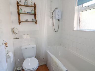 A bathroom with a toilet a bathtub with a shower and a wooden wall shelf with decor at Studland Cottage in Studland