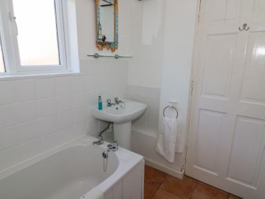 A bathroom with a bathtub sink mirror towel ring and a door at Studland Cottage in Studland