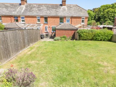 A garden with grass lawn and flowers next to a wooden fence behind a brick house at Studland Cottage in Studland