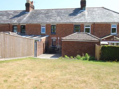 A backyard with a lawn patio furniture and a brick shed behind a row of connected brick houses at Studland Cottage in Studland