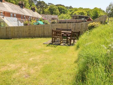 A garden with wooden chairs and a table on a grassy lawn surrounded by a wooden fence at Studland Cottage in Studland