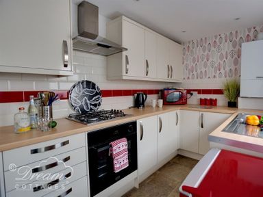 A kitchen with white cabinets red microwave and kettle a gas stove and patterned wallpaper at Sunny Days in Weymouth