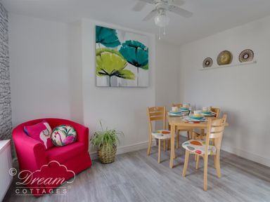 A dining area with wooden table and chairs with patterned cushions a red armchair with cushions and a plant in a woven basket at Sunny Days in Weymouth