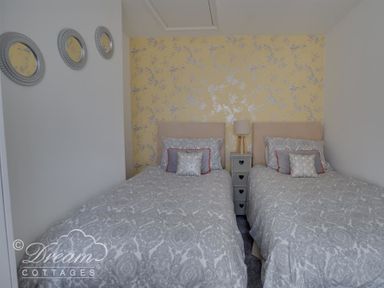 A bedroom with two single beds with patterned bedding a nightstand with a lamp and round mirrors on the wall at Sunny Days in Weymouth