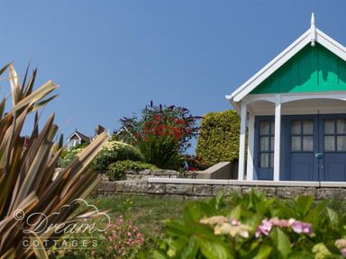 A garden with flowering plants and a small building with blue doors and a green gable at Sunny Days in Weymouth