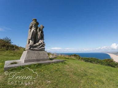 Stone sculpture of three fishermen on a grassy hill overlooking the sea and beach at Sunny Days in Weymouth