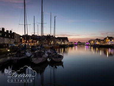 Boats docked along a waterfront with buildings and lights at dusk at Sunny Days in Weymouth