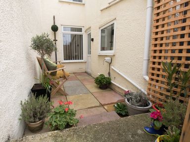 A small patio area with potted plants wooden bench with cushions and a wooden trellis at Sunny Days in Weymouth