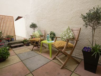 A small outdoor patio with two wooden chairs with cushions and a small green table between them at Sunny Days in Weymouth