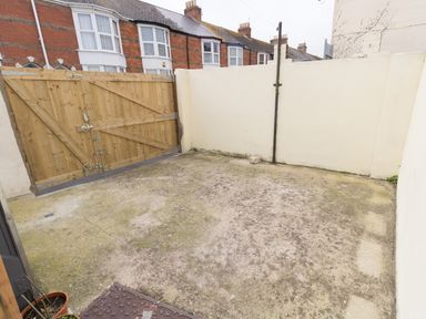 A concrete enclosed yard with a wooden gate and adjoining white walls at Sunny Days in Weymouth