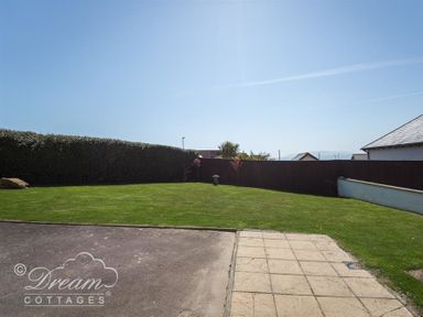 A garden with grass hedge and tiled patio at Tides Corner in Bowleaze