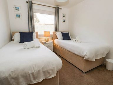 Two single beds in a bedroom with curtains and a lamp at Tides Corner Bowleaze